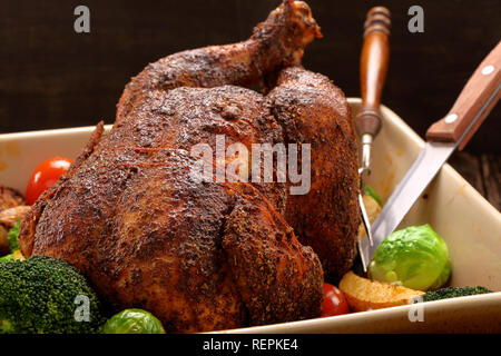 Ganze gegrillte Hühnchen mit Gemüse in Schüssel auf hölzernen Hintergrund Stockfoto