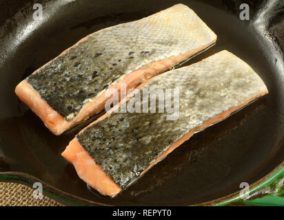 In der Nähe von zwei roher Lachs Fischfilets Haut nach oben in Gusseisen Bratpfanne beschichtet in Olivenöl Stockfoto