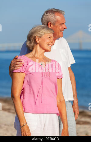 Gerne älterer Mann und Frau Paar ständigen Umarmen im Urlaub auf einer einsamen weißen Sandstrand mit hellen, klaren, blauen Himmel und ruhige See Stockfoto