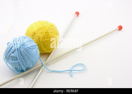 Zwei Kugeln aus Wolle, ein Gelb und das andere blau, neben der Stricknadeln Stockfoto