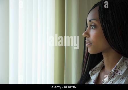 Schöne junge dunkelhäutige Frau durch ein Fenster mit einem nachdenklichen Ausdruck Stockfoto