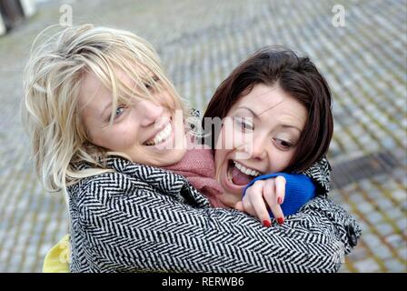 Zwei junge Frauen lachen und mit Freude umarmen Stockfoto