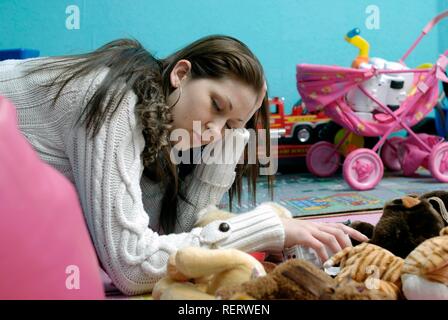 Eine müde Junge Mutter ruht für einen Moment vor dem Aufräumen unordentlich Ihrer Kinder Spielzimmer Stockfoto