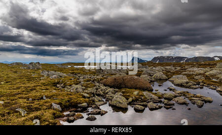 Ein Blick auf die felsigen und steinigen Gelände mit stürmischen Wolken mit Bergen im Hintergrund. Norwegen, um Beitostolen. Stockfoto