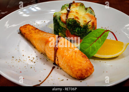 Gebackenes Lachsfilet mit einer Scheibe Zitrone, Mangold und Brokkoli und andere Gemüse mit Käse Stockfoto