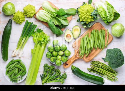 Vegan Konzept. Verschiedene Zutaten, grünes Gemüse am weißen Tisch brokkolisprößlinge Erbsen avocado Zucchini Bohnen Bok choy Sellerie, Ansicht von oben Stockfoto
