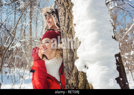 Verspieltes Paar versteckt sich hinter einen Baum im Schnee Stockfoto