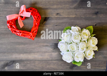 Ein Blumenstrauß aus den weißen Rosen und einem Herz aus roten auf einem hölzernen Hintergrund. Romantische Karte Konzept. Die Aussicht von oben. Flach. Stockfoto