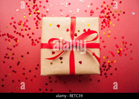 Geschenkbox in braun gefärbte Handwerk Papier gewickelt und mit roter Schleife auf dunklem Hintergrund rot mit rotem Konfetti gebunden. Stockfoto