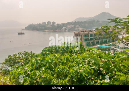 Grüne Blätter im Überfluss an Bäumen in Aussichtspunkt mit Blick auf das Meer mit dem Boot auf dem Wasser in Hongkong, China, über dunstige Tag in einer asiatischen Stadt. Stockfoto