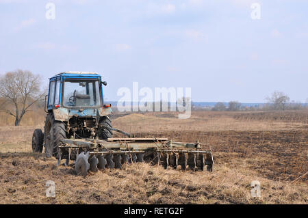 Leere blaue spritzt - Traktor mit rostigen Egge auf dem Feld im Frühjahr Stockfoto