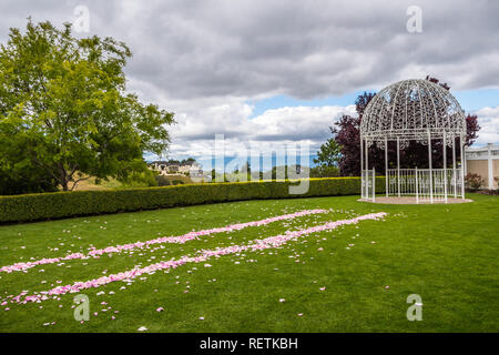 Im Freien Hochzeit mit geschmiedeten Eisen Hochzeit arch und Rosenblätter verteilt auf grünem Rasen; bewölkter Himmel Hintergrund Stockfoto