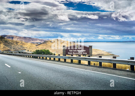 Fahrt durch die goldenen Hügel von Kalifornien; der San Luis Reservoir State Recreation Area unterzeichnen und Damm auf der rechten Seite der Straße. Stockfoto