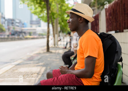 Junge glücklich schwarzen Afrikanischen touristische Mann an der Bushaltestelle sitzen Stockfoto