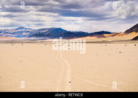 Verschieben von Felsen und ihre Spuren am Racetrack Playa, Berge und Wolken Landschaft im Hintergrund; Death Valley National Park, Kalifornien Stockfoto