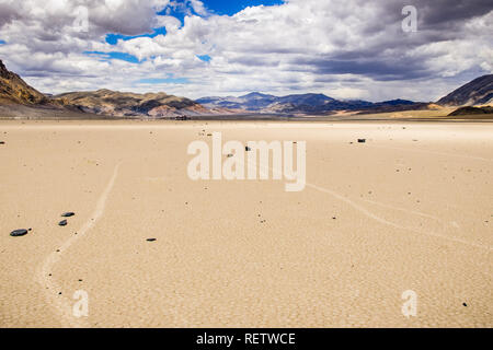 Verschieben von Felsen und ihre Spuren am Racetrack Playa, Berge und Wolken Landschaft im Hintergrund; Death Valley National Park, Kalifornien Stockfoto