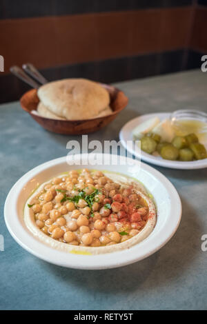 In einem israelischen Mittagessen im Café in Tel Aviv, Israel. Cremigen Hummus mit ganzen cheakpeas Nahaufnahme, Haufen von Pitas und Pickles auf dem Hintergrund Stockfoto