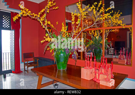 Große grüne Vase mit gelben Blüten und rote Kerzen auf dem Tisch, Spiegel an der Wand, Boden, Rot innen Marvel Stockfoto