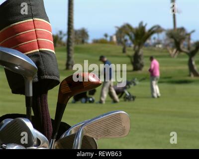 Golfspieler und Push Golfcaddys auf Golfplatz mit Palmen. Eine Tüte Golf Clubs im Vordergrund gesehen. Stockfoto