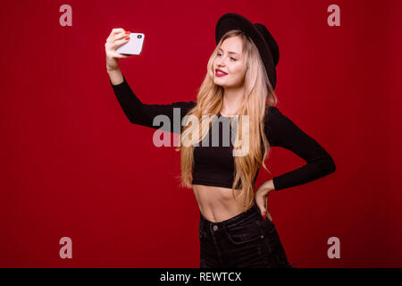 Cool elegant Woman in Black t-shirt und Hut nehmen selfie auf Ihr Handy über den roten Hintergrund isoliert Stockfoto