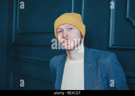 Attraktive nach bärtigen Mann Hipster in gelben Hut misstrauisch an Kamera auf der blauen Wand Hintergrund Stockfoto