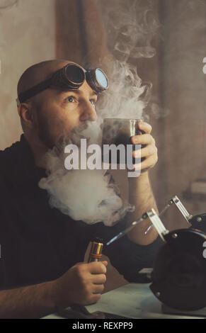 Master raucht und Getränke heiße Getränke in der Pause. Mann in Gläser in Gedanken hält Becher in der Hand und lässt Sie rauchen. Er raucht eine elektronische Zigarette. Stockfoto