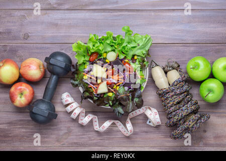 Blick von oben auf die gesunde Lebensweise Konzept, Kurzhanteln, Seil springen, Äpfel und frische Salat auf Holz Hintergrund. Ansicht von oben mit der Kopie. Stockfoto