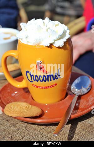Eine heiße Schokolade trinken in einer Chocomel Tasse, garniert mit Sahne und mit einem Keks an der Seite, serviert im Freien unter der Sonne. Stockfoto
