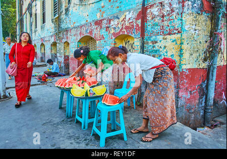 YANGON, MYANMAR - Februar 17, 2018: Spontane Handel in Chinatown - Frauen verkaufen Scheiben rote und gelbe Wassermelonen aus den Fächern, stehend auf dem Stockfoto