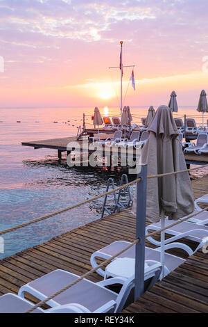 Blick auf den romantischen Sonnenaufgang Himmel, Meer und Plattform mit leeren Liegestühlen und Sonnenschirmen. Stockfoto