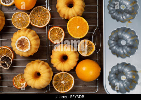 Kleine orange bundt Kuchen mit frischen und trockenen Orangen auf Kühlung ruck, indem auf Schimmel, Ansicht von oben, flach Stockfoto