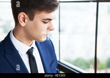 Porträt einer umgekippt und Sorgen junger stattlicher Geschäftsmann stand in der Nähe der Fenster. Stockfoto