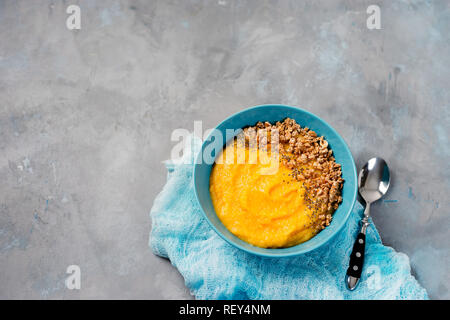 Blick von oben auf die gelben Smoothie Schüssel mit Müsli in blauen Platte Stockfoto