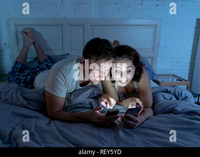 Lächelnd attraktive junge Männer und Frau Paar mit Smartphone auf dem Bett zusammen liegen. Gerne Freund und Freundin Kontrolle soziale Netzwerke oder mobil Stockfoto