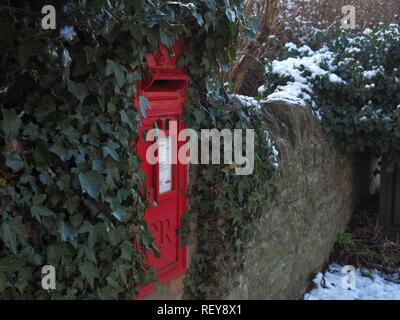 Eine rote Post Box in eine Mauer aus Stein im Schnee in Forest Hill, Oxfordshire eingestellt Stockfoto