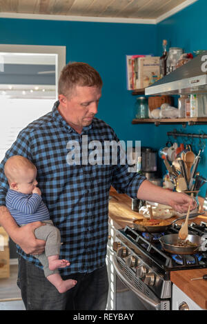 Denver, Colorado - Adam Hjermstad Sr. Köche eine Mahlzeit während seiner vier Monate alten Sohn, Hendrix. Stockfoto