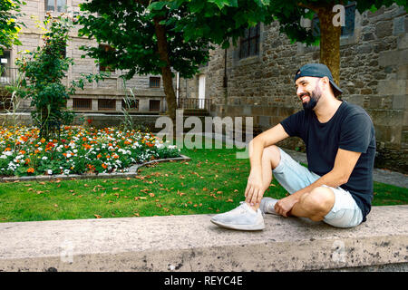 Porträt eines Mannes mit Bart und "SNAPBACK", in der Straße weg schauen sitzend, fröhlicher, entspannter, Genuss, Freizeit Konzept. Stockfoto