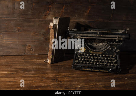 Lesen und Schreiben von Szenen in alten Zeiten: ein altes Buch und eine alte Schreibmaschine auf einem zerstörten Holztisch auf einer hölzernen Hintergrund Stockfoto