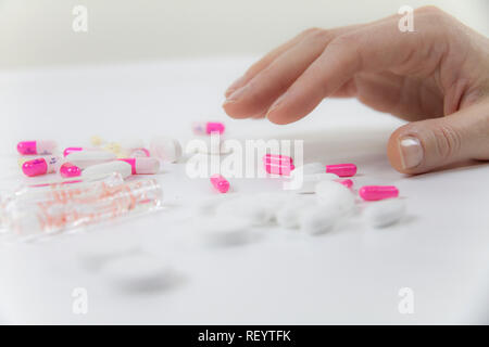 Die Abhängigkeit von Medikamenten und Drogen in modernen Zeiten: Nahaufnahme der Hand einer jungen Frau über die verschiedenen Tabletten und Ampullen auf Tisch und weiß bac Greifer Stockfoto