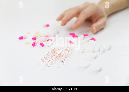 Die Abhängigkeit von Medikamenten und Drogen in modernen Zeiten: Nahaufnahme der Hand einer jungen Frau über die verschiedenen Tabletten und Ampullen auf Tisch und weiß bac Greifer Stockfoto