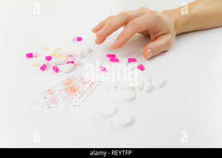 Die Abhängigkeit von Medikamenten und Drogen in modernen Zeiten: Nahaufnahme der Hand einer jungen Frau über die verschiedenen Tabletten und Ampullen auf Tisch und weiß bac Greifer Stockfoto