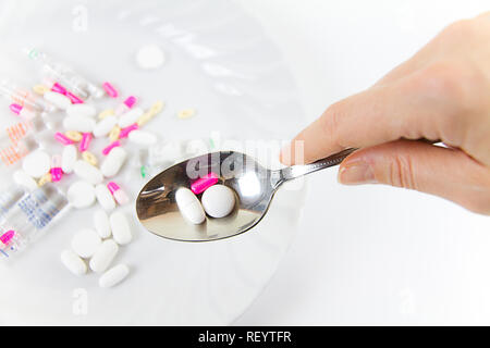 Die Abhängigkeit von Medikamenten und Drogen in modernen Zeiten: eine Hand von einer jungen Frau mit einem Esslöffel Tabletten aus einem Teller voll von Medikamenten auf das Weiße Registerkarte Stockfoto