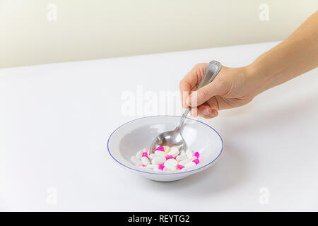 Die Abhängigkeit von Medikamenten und Drogen in modernen Zeiten: eine Hand von einer jungen Frau mit einem Esslöffel Tabletten aus einem Teller voll von Medikamenten auf das Weiße Registerkarte Stockfoto