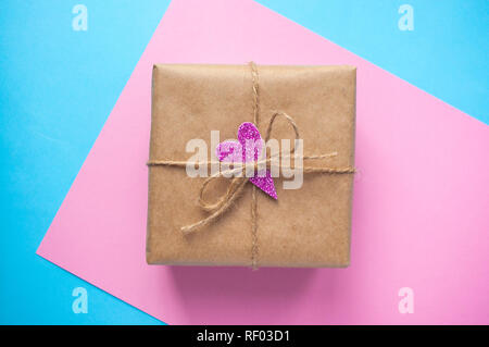 Geschenkbox in Handwerk Papier mit Rosa glitzerndes Herz gewickelt und gebunden mit Seil auf Blau und Rosa Hintergrund. Stockfoto