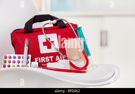 Nahaufnahme eines Erste Hilfe Kit neben bunten Pillen, Spritzen, Stethoskop und sterile Bandagen auf einem weißen Stuhl in einem medizinischen Zentrum Stockfoto