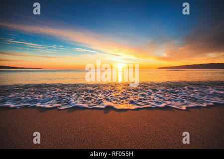 Schönen Sonnenaufgang über dem Meer. Wellen waschen Sandstrand Stockfoto