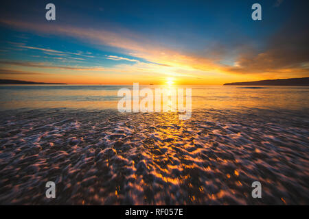 Schönen Sonnenaufgang über dem Meer. Wellen waschen Sandstrand Stockfoto