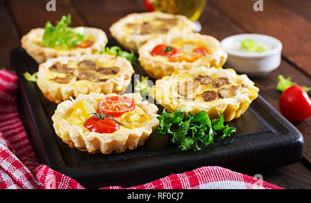 Pilze, Cheddar, Tomaten Törtchen auf Holz- Hintergrund. Mini Torten. Leckere Vorspeisen, Tapas, Snacks. Stockfoto