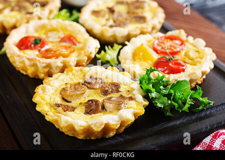 Pilze, Cheddar, Tomaten Törtchen auf Holz- Hintergrund. Mini Torten. Leckere Vorspeisen, Tapas, Snacks. Stockfoto