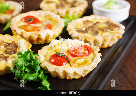 Pilze, Cheddar, Tomaten Törtchen auf Holz- Hintergrund. Mini Torten. Leckere Vorspeisen, Tapas, Snacks. Stockfoto